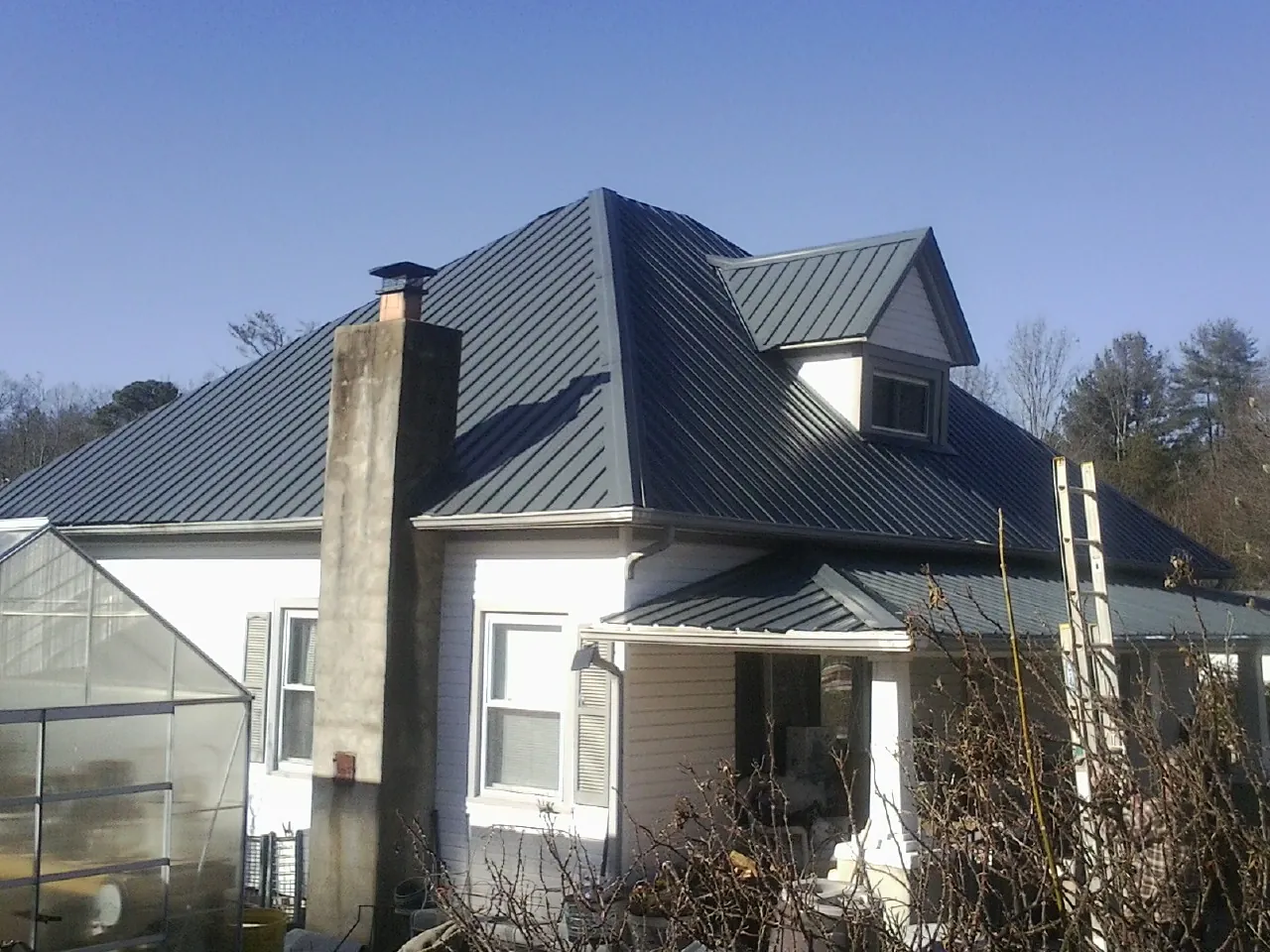 Dark blue standing seam metal roof on a white farmhouse with dormer — Slate & Tile Roof Repair by Roofing Brothers in Clyo