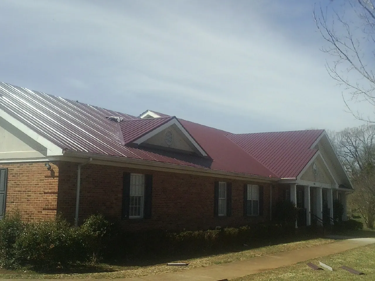Red metal roof with gabled entries on a long brick building, from a Hail Damage Roof Repair job in Clyo