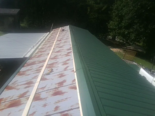 Old rusted panels beside newly installed green metal roofing — Wind Damage Roof Repair by Roofing Brothers in Clyo