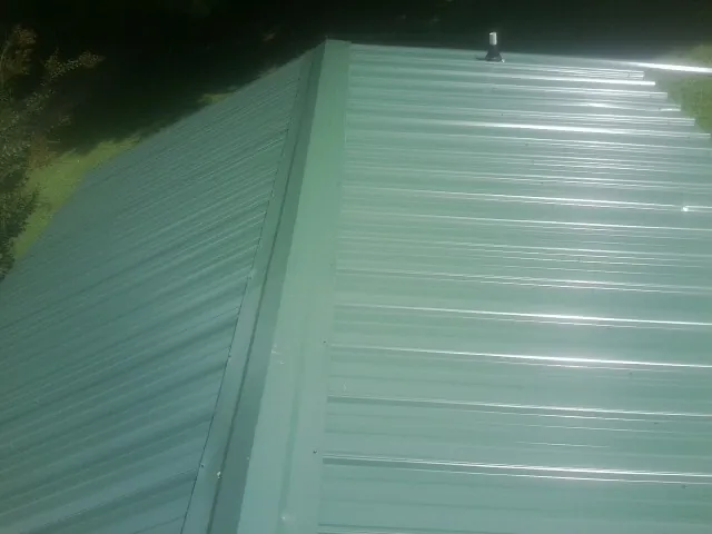 New green metal panels meeting at the ridge of a roof — Flat Roof Repair work by our crew in Clyo