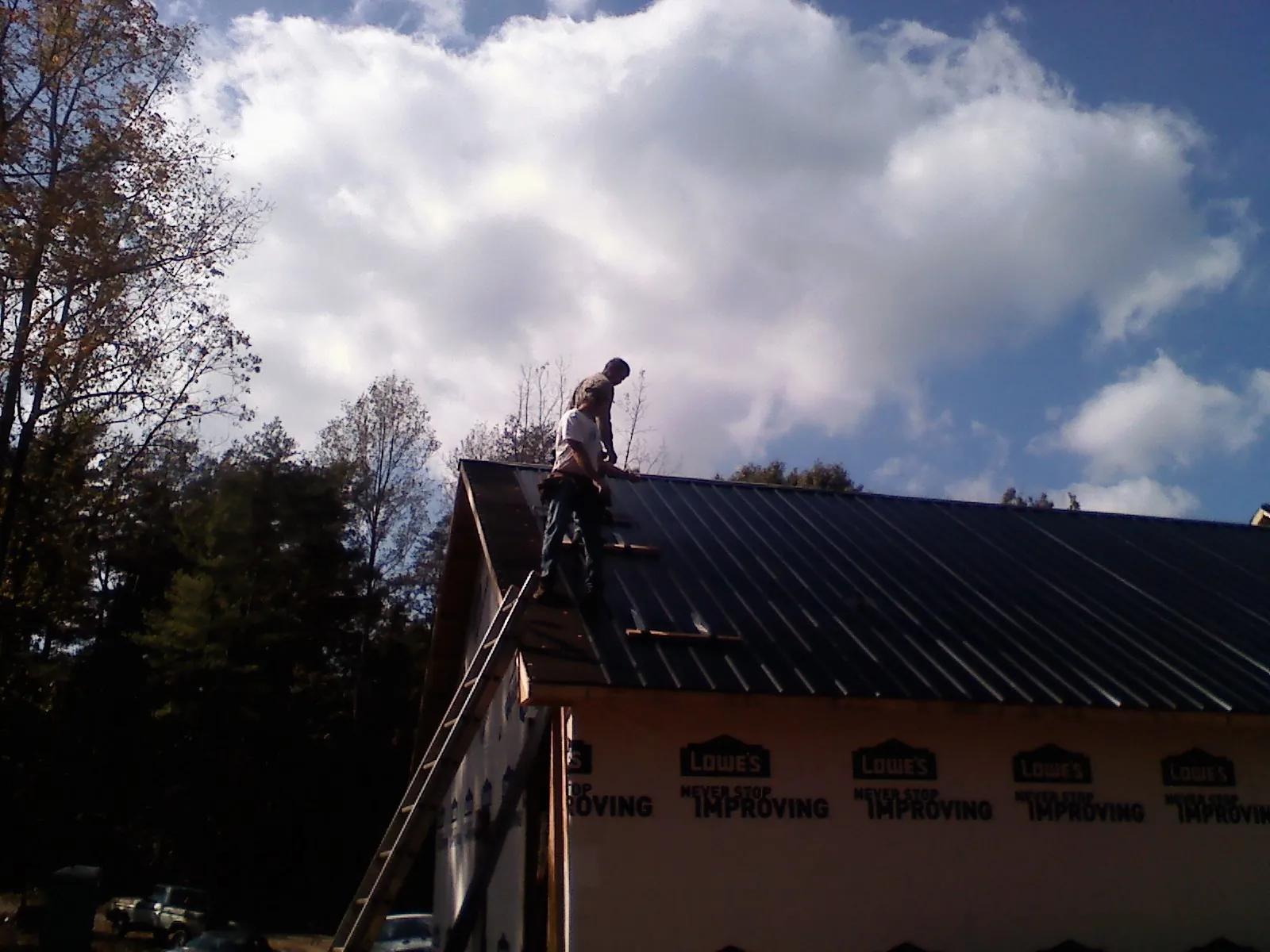 Roofer fastening dark metal panels high against a cloudy sky, from a Roof Inspection job in Clyo
