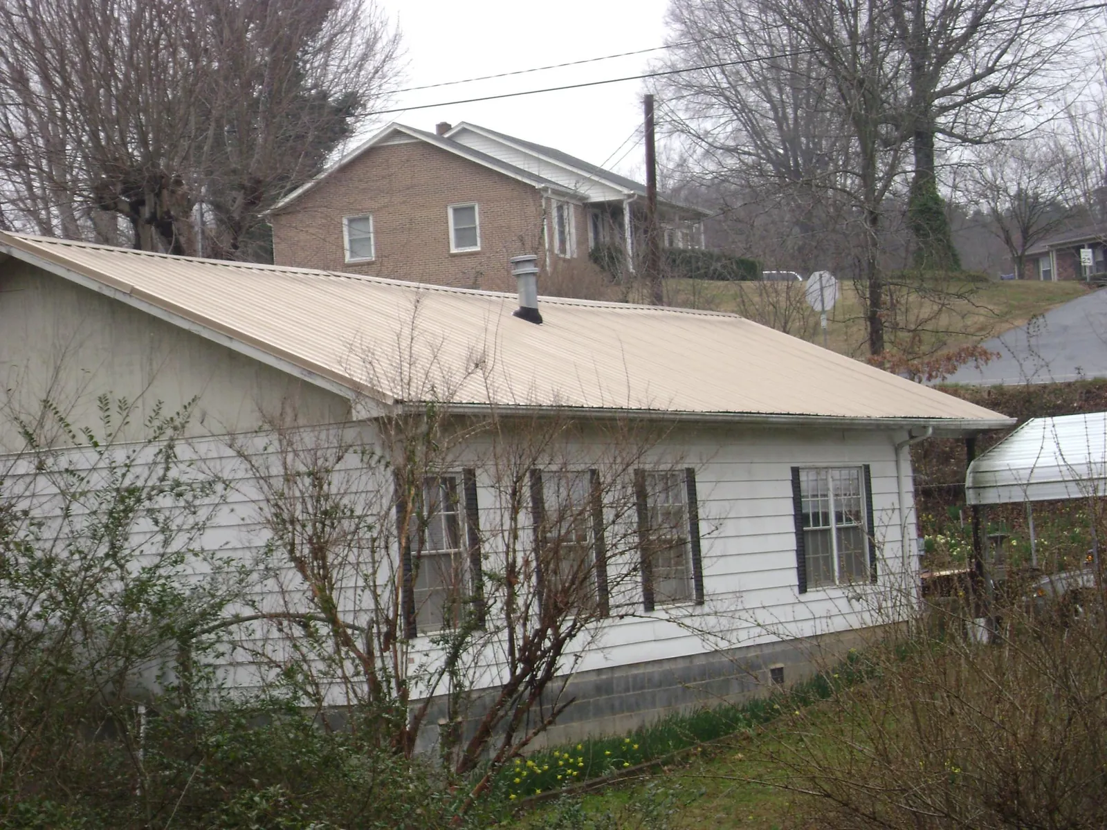 Tan metal roof on a white sided house set into a hillside — Commercial Roofing by Roofing Brothers in Clyo